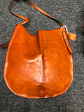 A large, crescent-shaped brown leather shoulder bag with a long strap