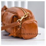 A close-up of a brown leather bag with gold-tone hardware, including a zipper, clasp, and wrist strap