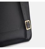 Close-up of a black pebbled leather bag corner with a gold-tone rectangular buckle and strap detail