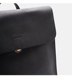 Close-up of a black pebbled leather backpack flap with a small gold metal snap button