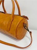 A close-up of a mustard yellow leather duffle bag with double top handles, a zippered closure