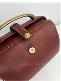Close-up of a burgundy leather handbag with gold-tone hardware, a top handle