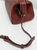 A close-up of a dark reddish-brown leather handbag showing the side profile