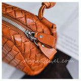 Close-up of a woven leather handbag in warm tan/cognac brown, showing a silver zipper, leather pull tab, and part of a top handle.