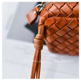 A close-up of a brown woven leather handbag strap with a matching leather tassel