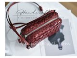 A small woven leather crossbody bag in a deep burgundy red, featuring a silver zipper and a matching leather strap