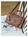 A brown leather handbag with a top handle, a diagonal zippered pocket, and a long shoulder strap