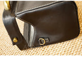 Close-up of a dark brown leather bag corner showing white contrast stitching, a zipper